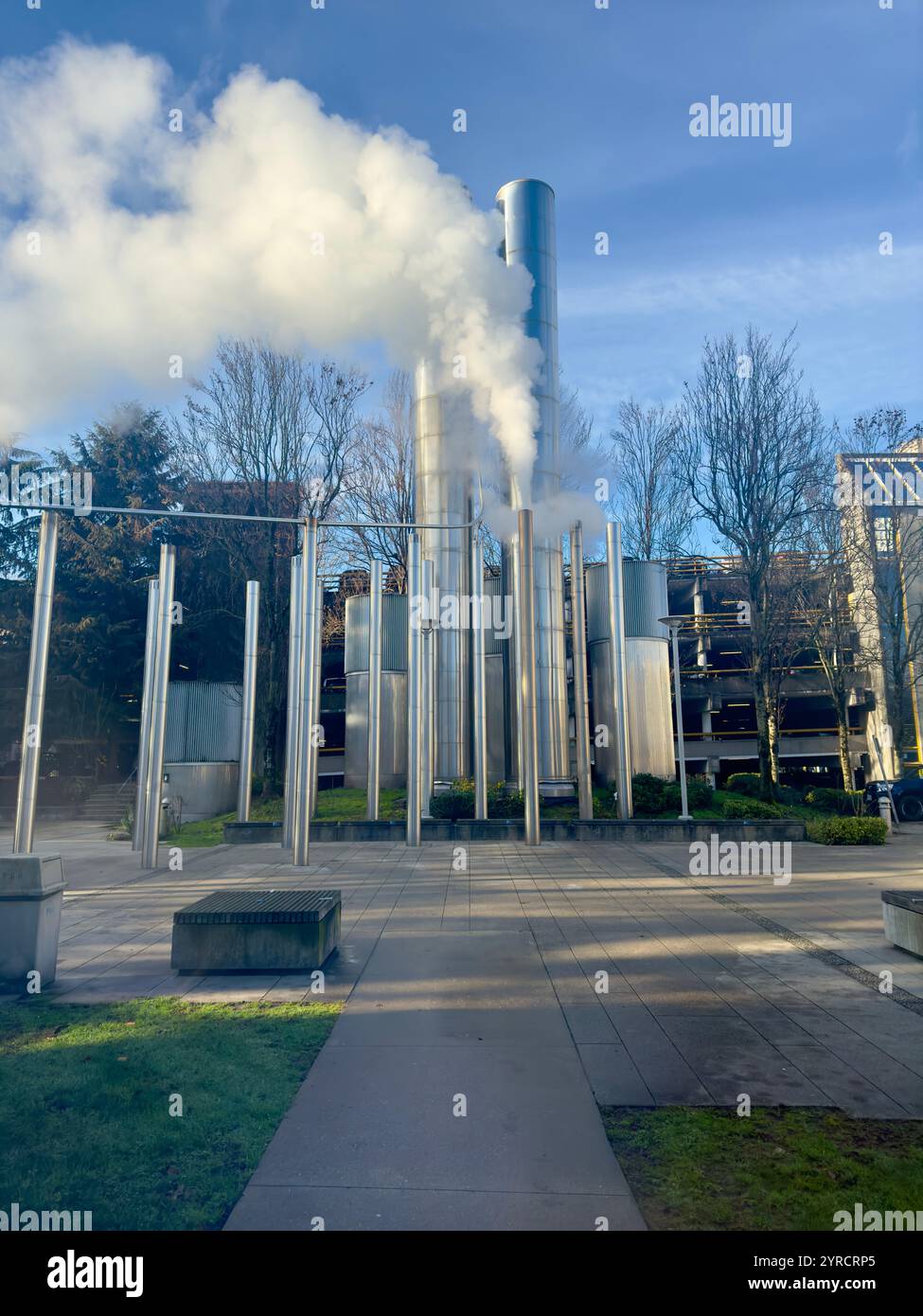 A modern industrial setup featuring tall metallic steam vents releasing vapor into a clear blue sky. - Smartphone Captured Stock Image