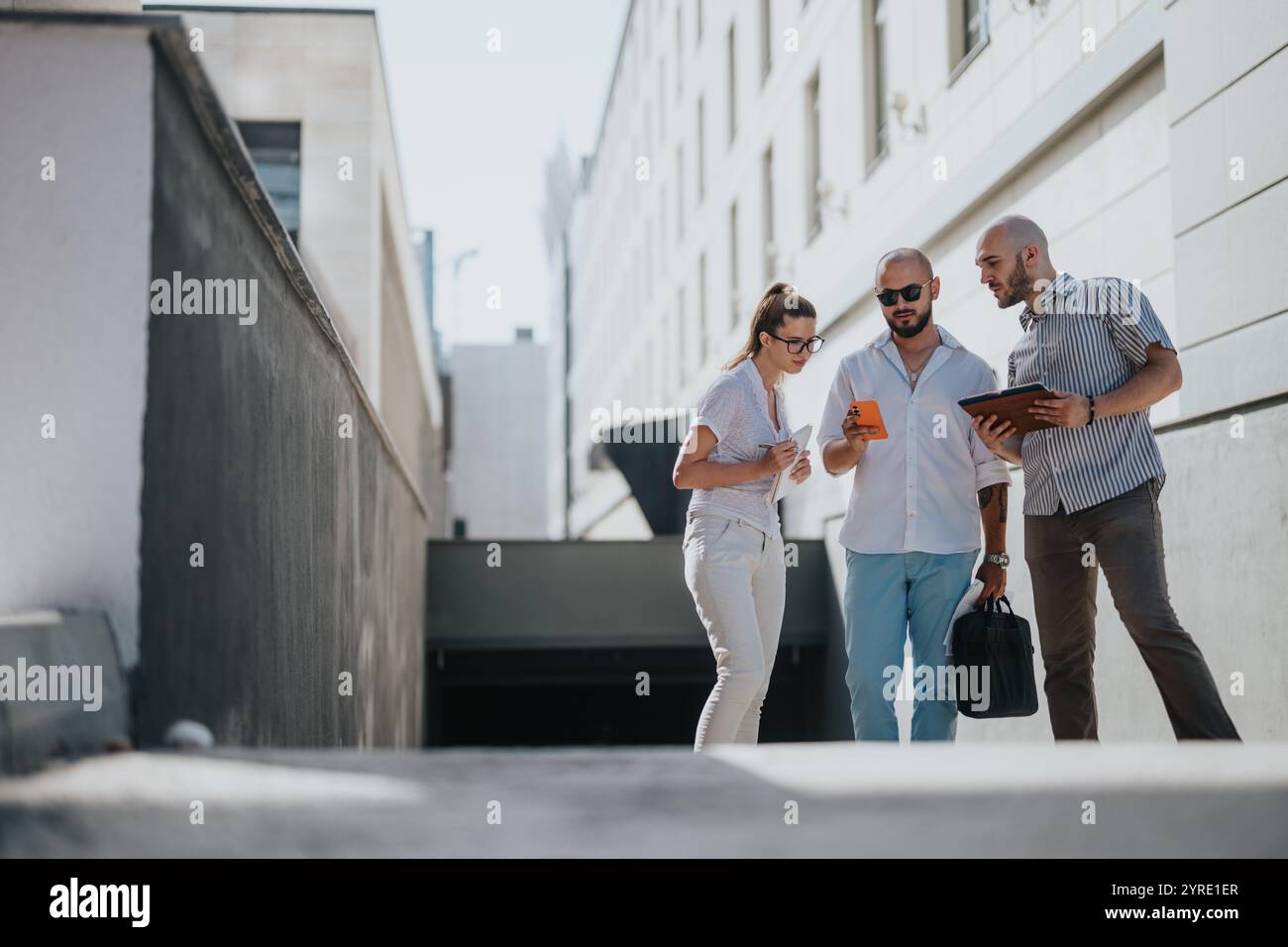 Business team collaborating outside modern office building while using digital devices Stock Photo