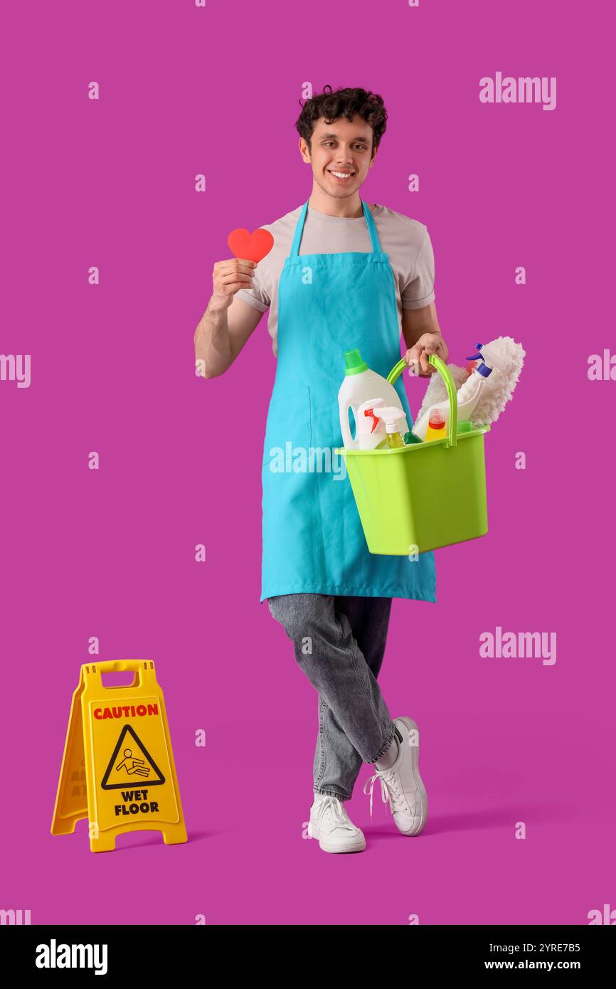 Happy male janitor with bucket of cleaning supplies, caution sign and ...