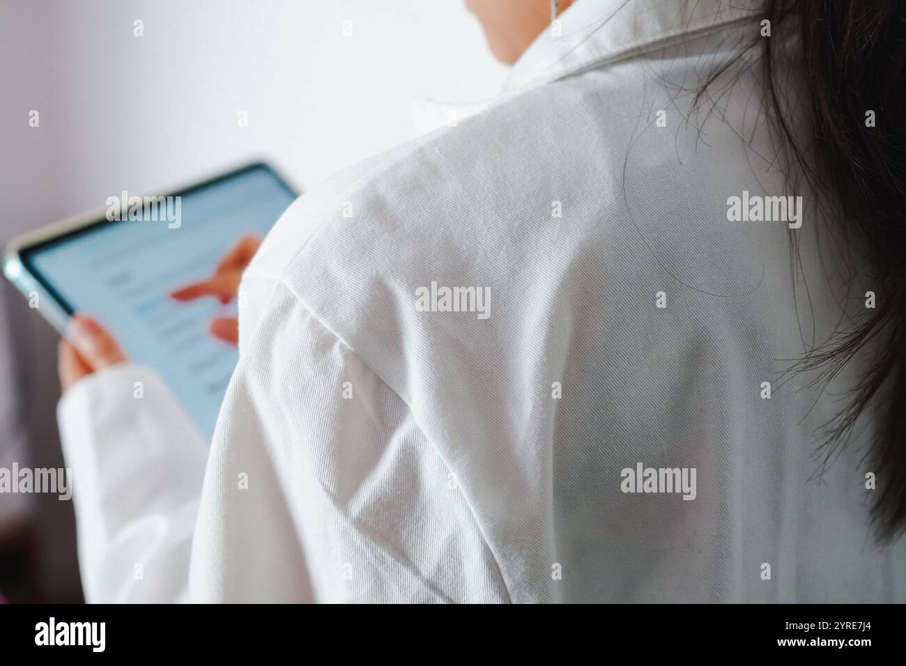 Close-up of the back of a young female doctor checking patient information on a tablet Stock Photo