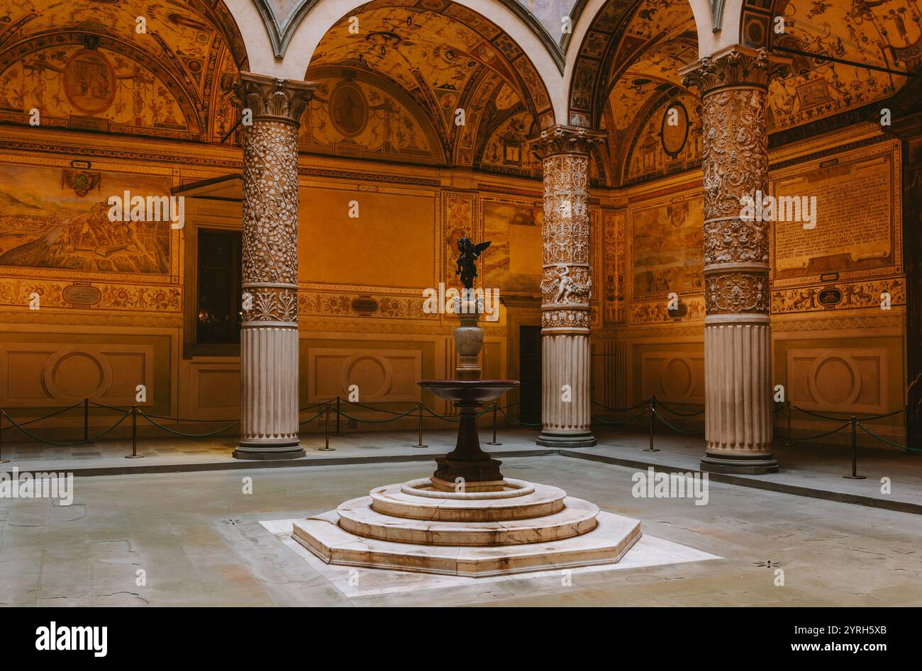 Warm light illuminates the ornate columns, intricate frescoes, and central fountain within the serene courtyard of palazzo vecchio, florence Stock Photo