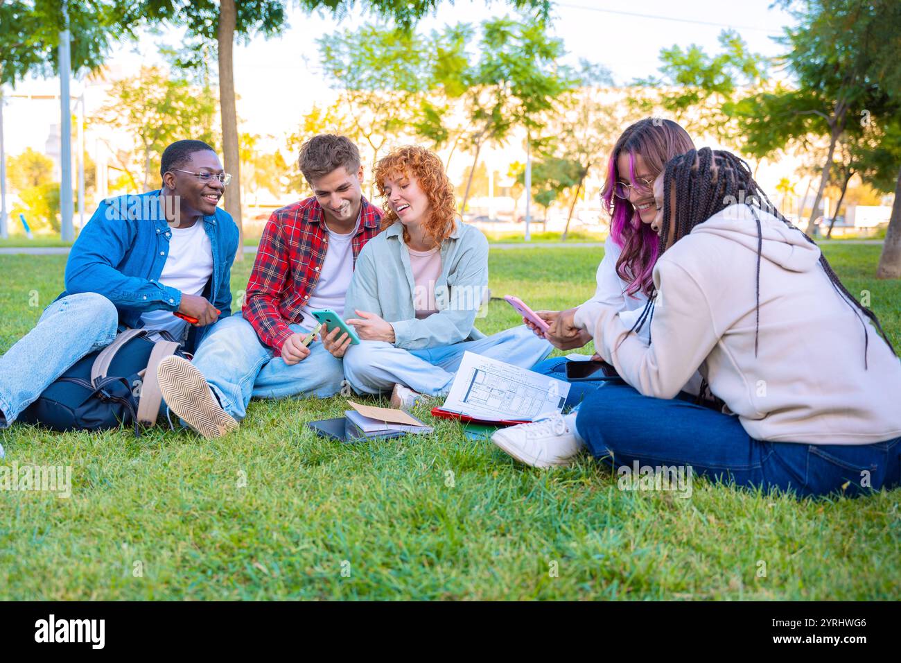 Group Young students using notebook together while sitting on grass outdoors Stock Photo