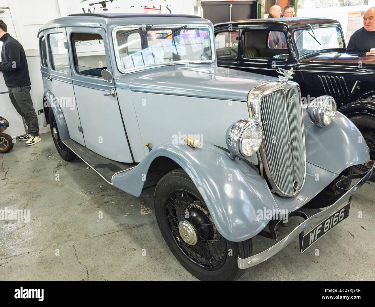 A classic vintage 1935 Jowett Kestrel car displayed indoors, showcasing its elegant design and polished details, surrounded by other antique vehicles - Smartphone Captured Stock Image