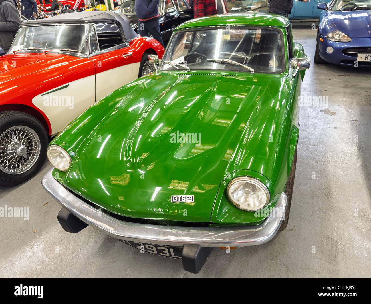Bright green classic triumph GT6 sports car in a showroom, parked among other vintage vehicles, showcasing sleek design and retro style - Smartphone Captured Stock Image