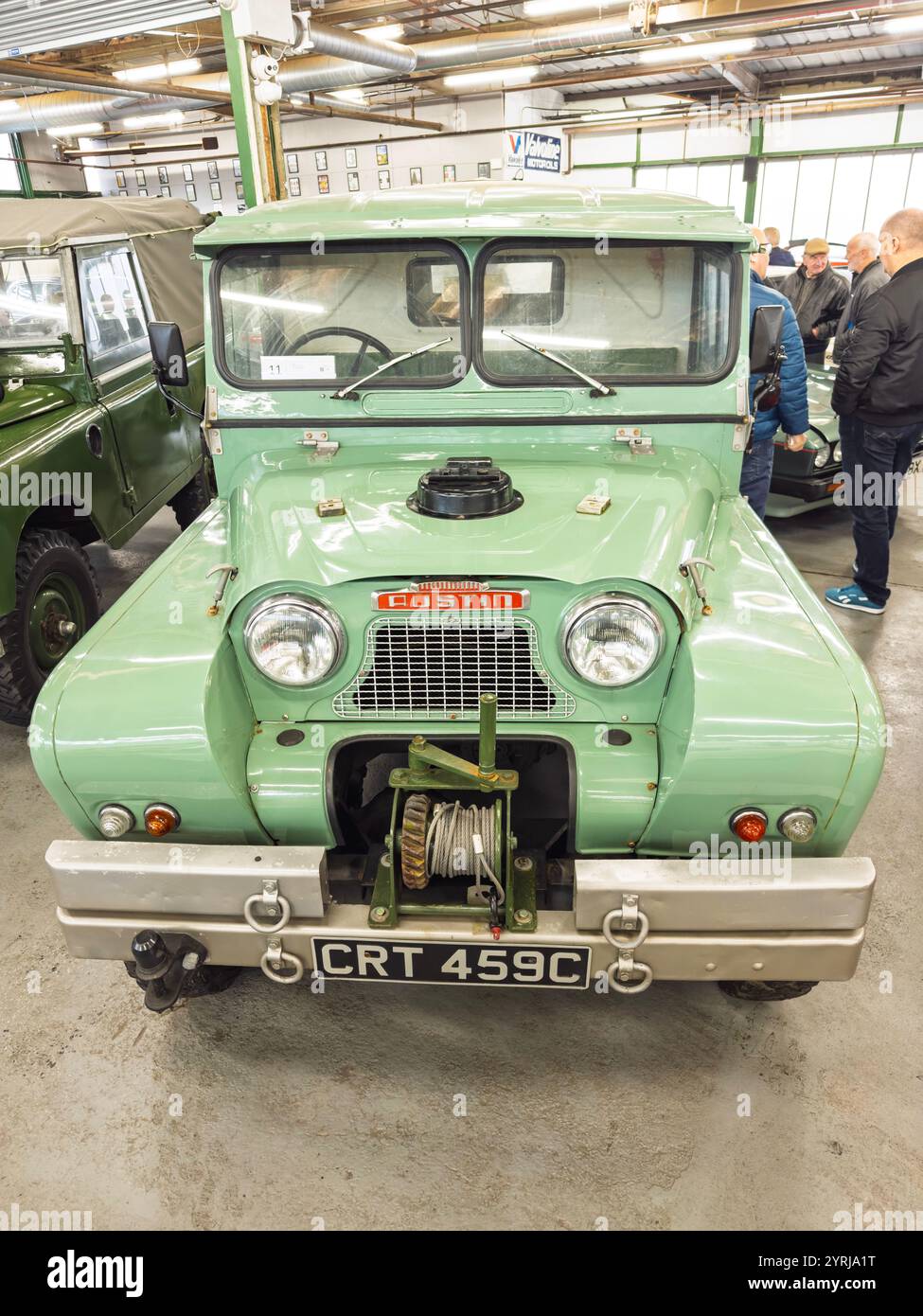 1965 Vintage light green Austin Gipsy vehicle with winch displayed at a classic car auction indoors with other vehicles and visitors in the background - Smartphone Captured Stock Image