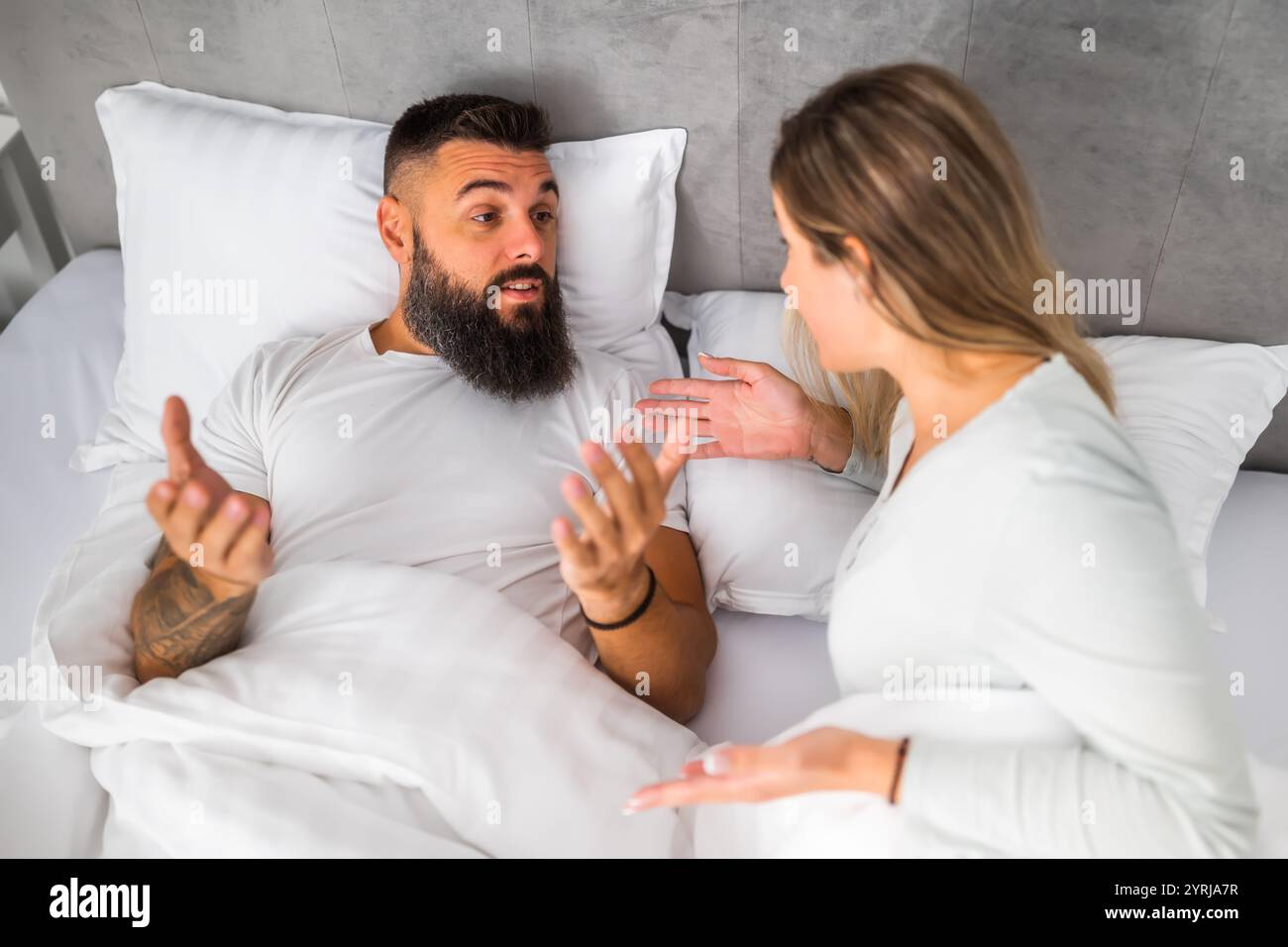 Couple is lying in bed and arguing. The woman is angry and offended and ...