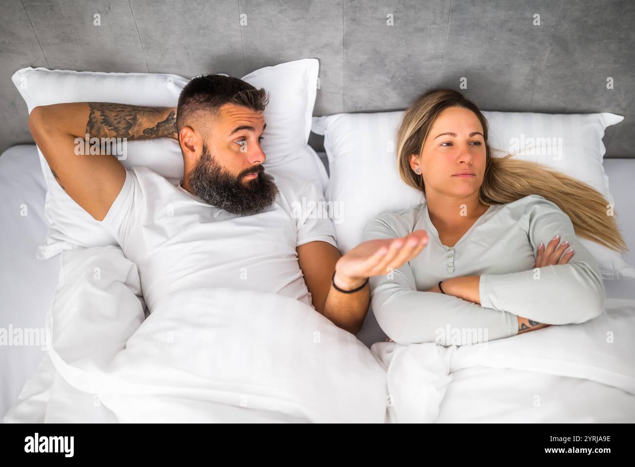 Couple is lying in bed and arguing. The woman is angry and offended and ...