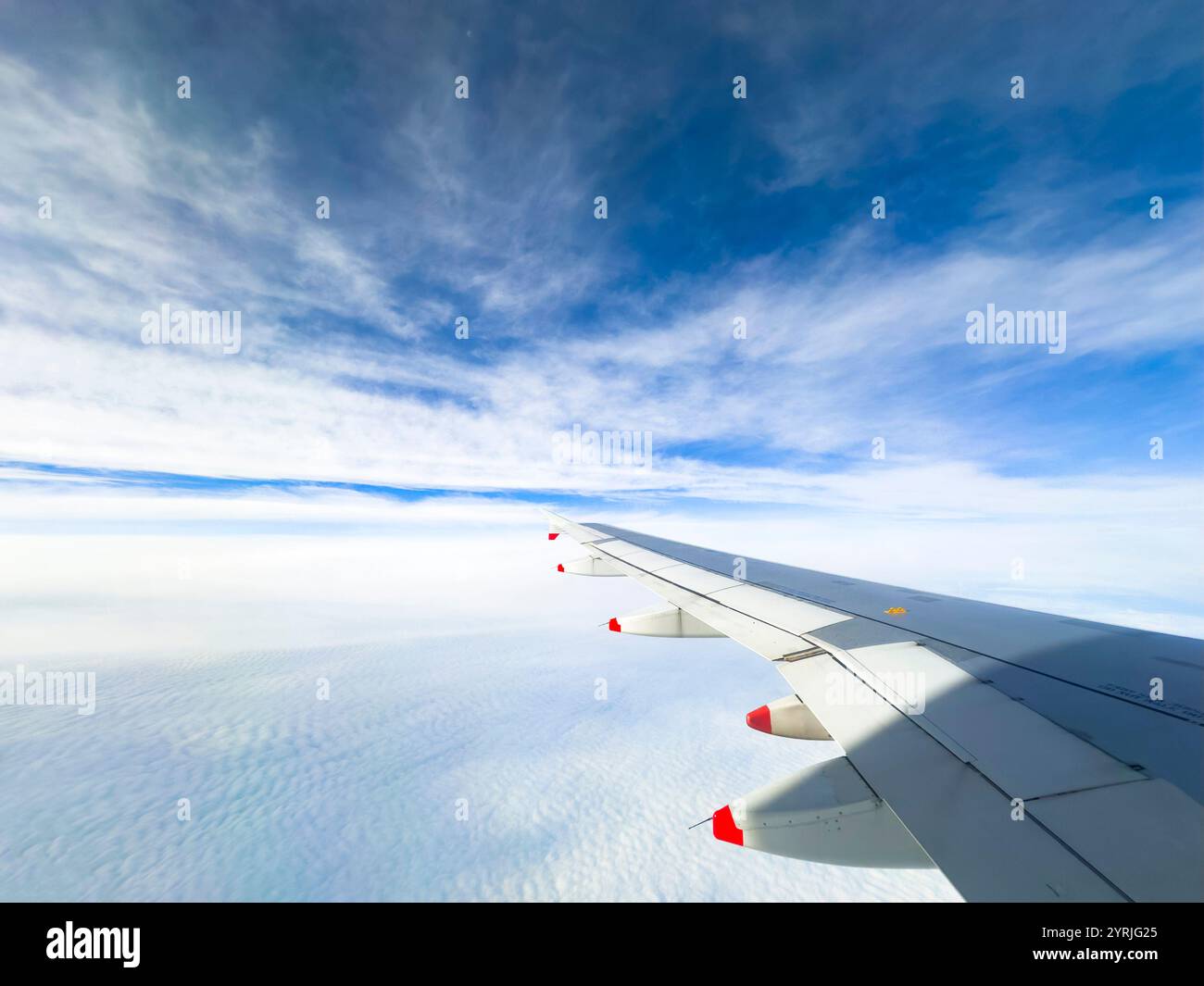 View of british airways airplane wing soaring above the clouds with a vibrant blue sky in the background - Smartphone Captured Stock Image