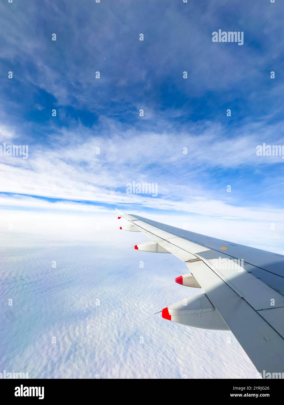 View of british airways airplane wing soaring above the clouds with a vibrant blue sky in the background - Smartphone Captured Stock Image
