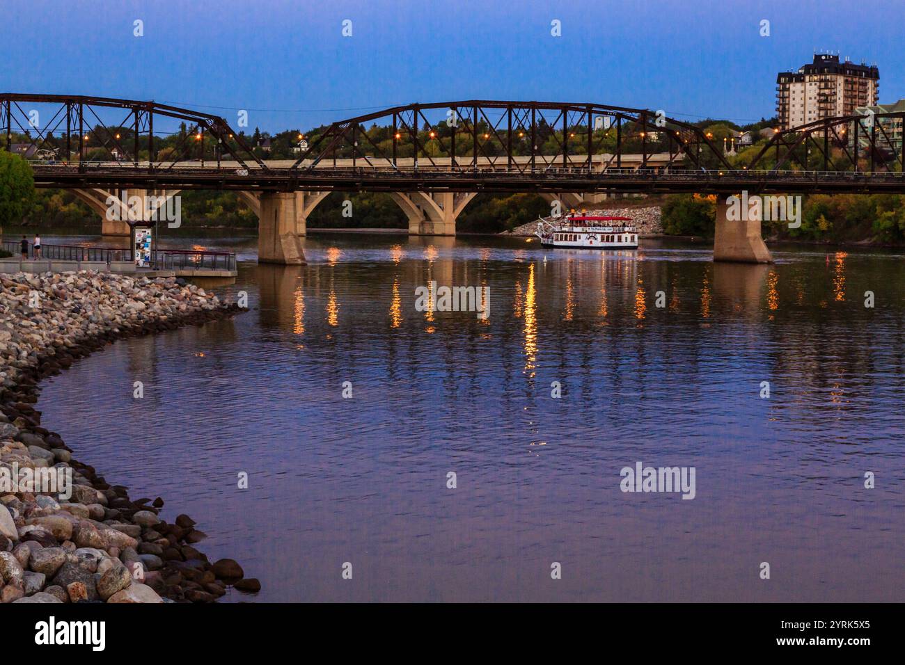 A bridge spans a river with a boat in the water. The bridge is lit up at night, creating a serene and peaceful atmosphere Stock Photo