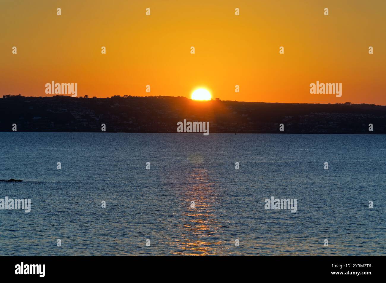 A dramatic autumnal sun setting on the coastline with reflections in sea at Mounts Bay Penzance Cornwall England UK Stock Photo