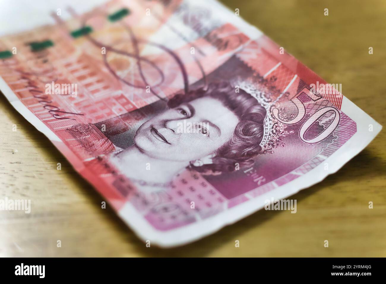 Close-up of a fifty-pound British banknote, featuring Queen Elizabeth II's portrait and architectural details.  The note is lying on a light brown woo Stock Photo