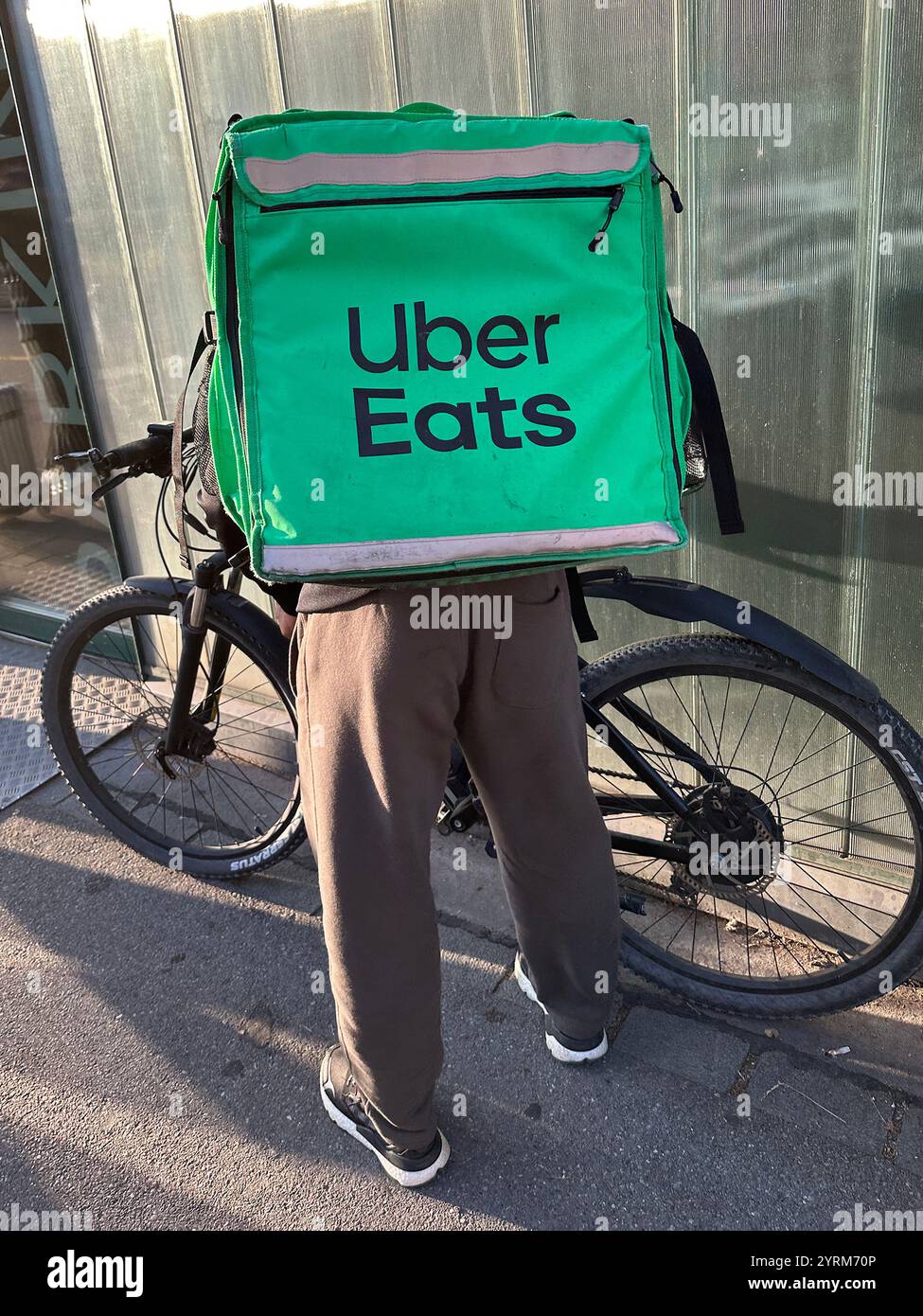 Zurich, Switzerland - June 27, 2023: An Uber Eats green bag is strapped to a food courier’s back, just before riding off for a delivery via bicycle. - Smartphone Captured Stock Image