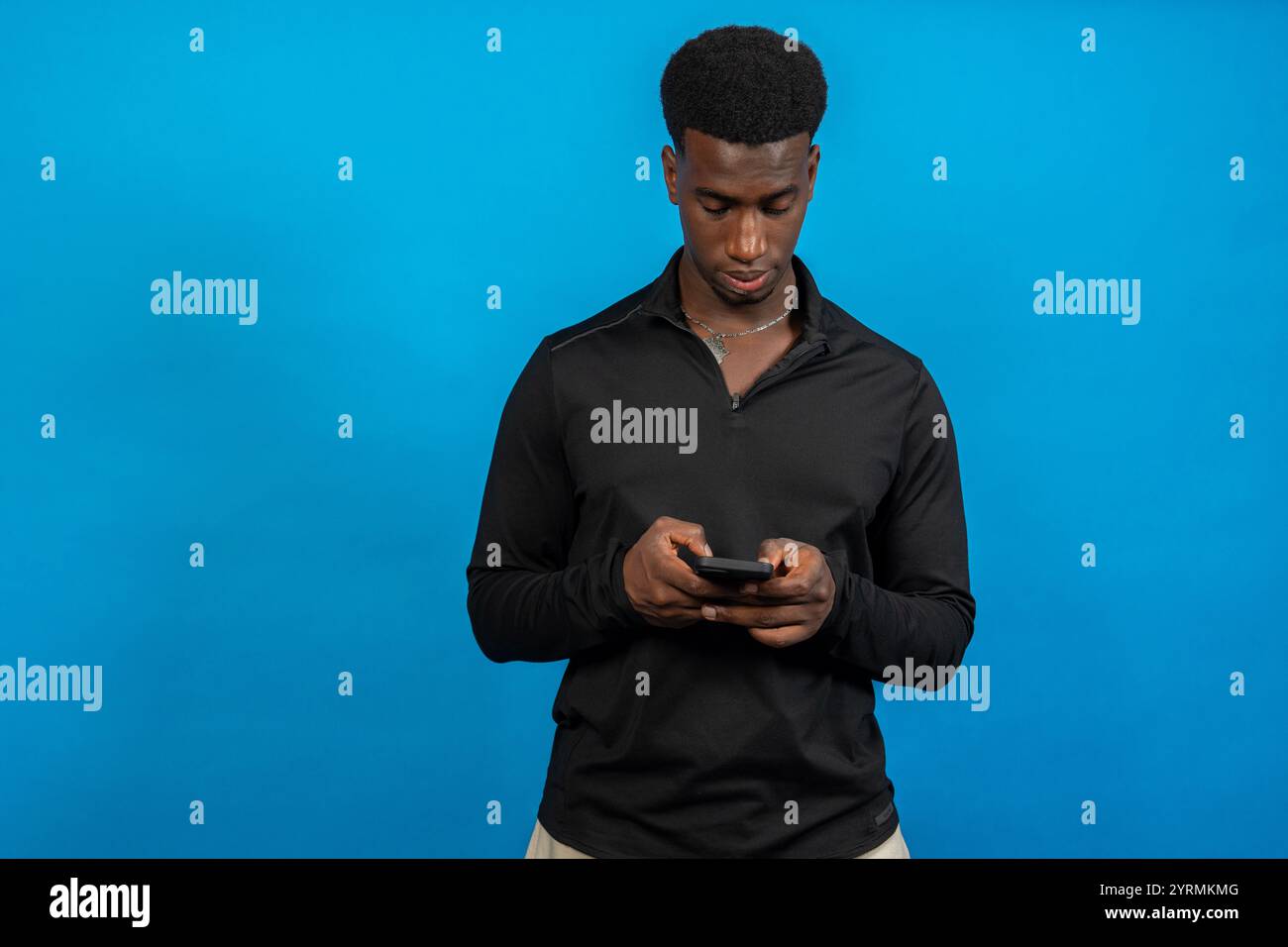 Young man using smartphone on blue background: concentrated young man using mobile phone Stock Photo