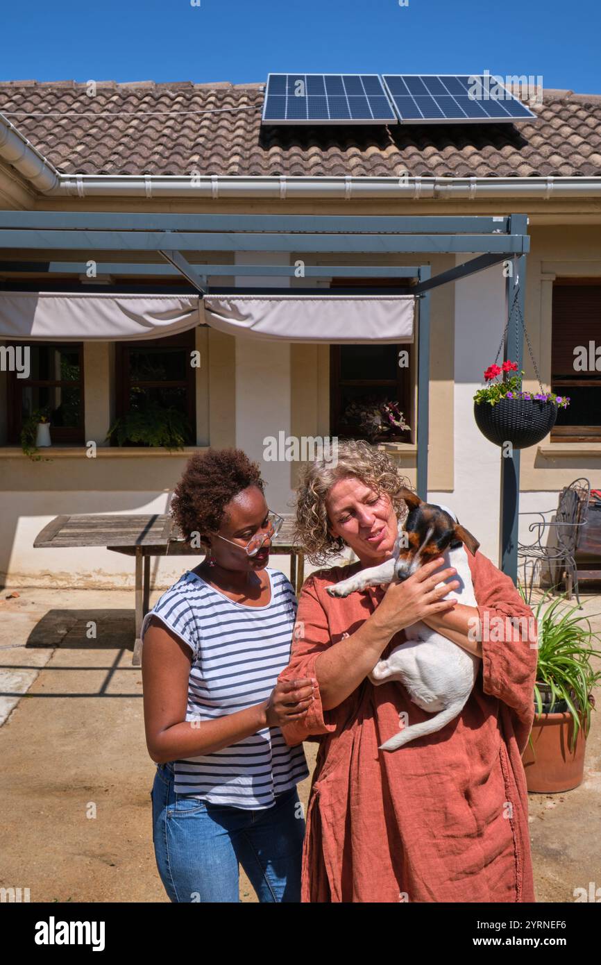 Two women smiling with a small dog in a backyard Stock Photo - Alamy
