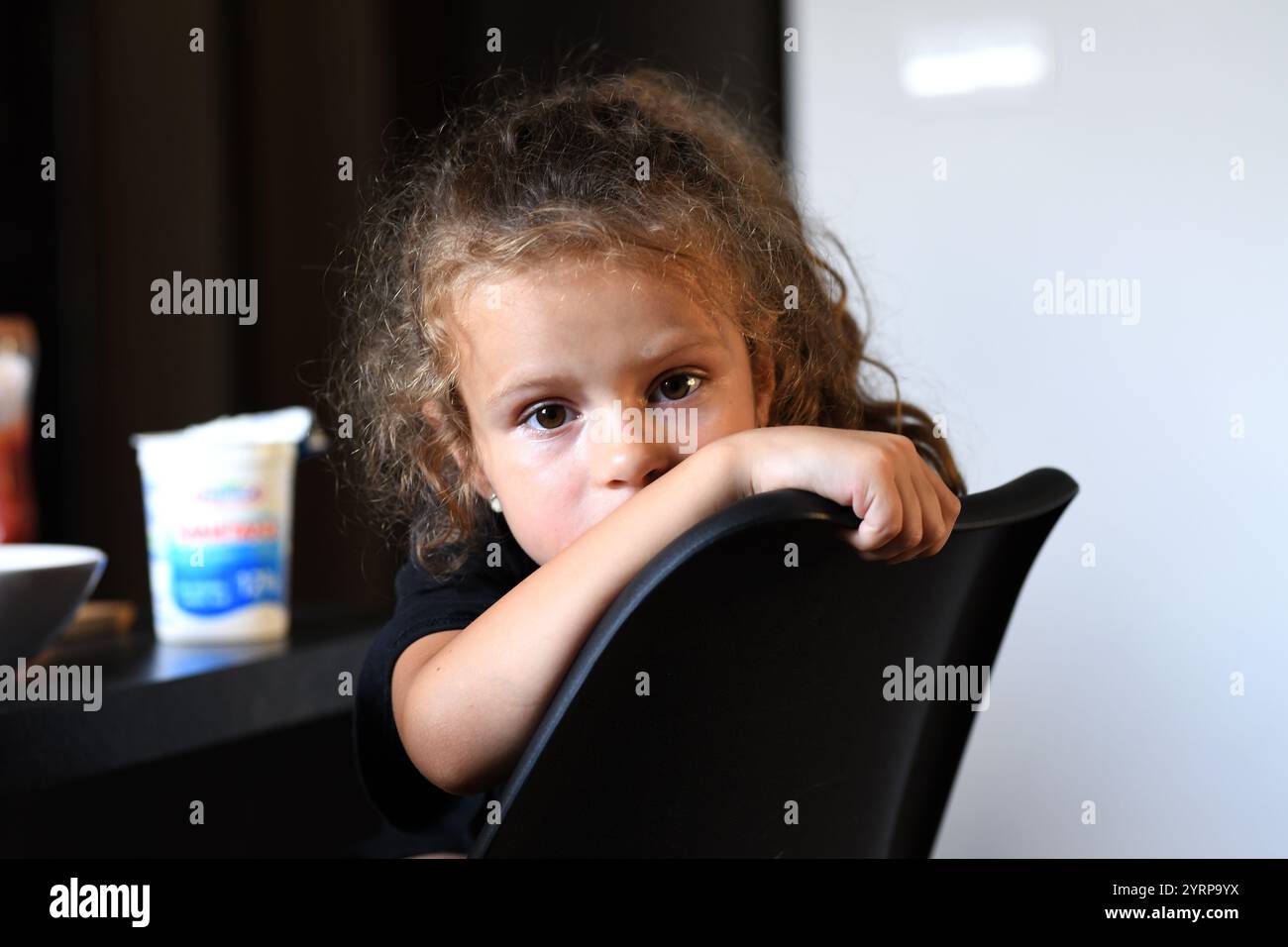 The image shows a little girl with curly hair sitting on a chair Stock ...