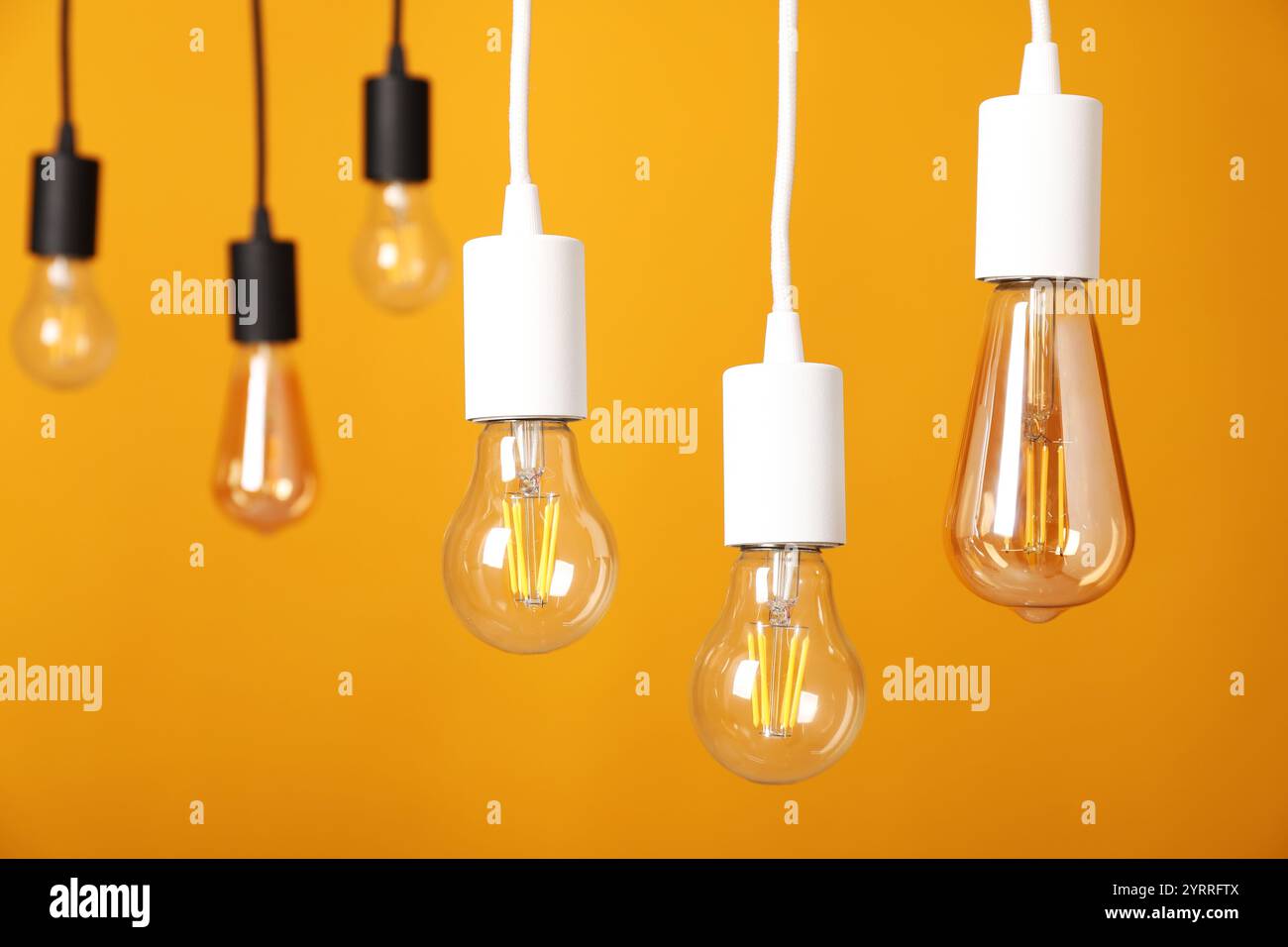 Light bulbs hanging on cords against orange background Stock Photo