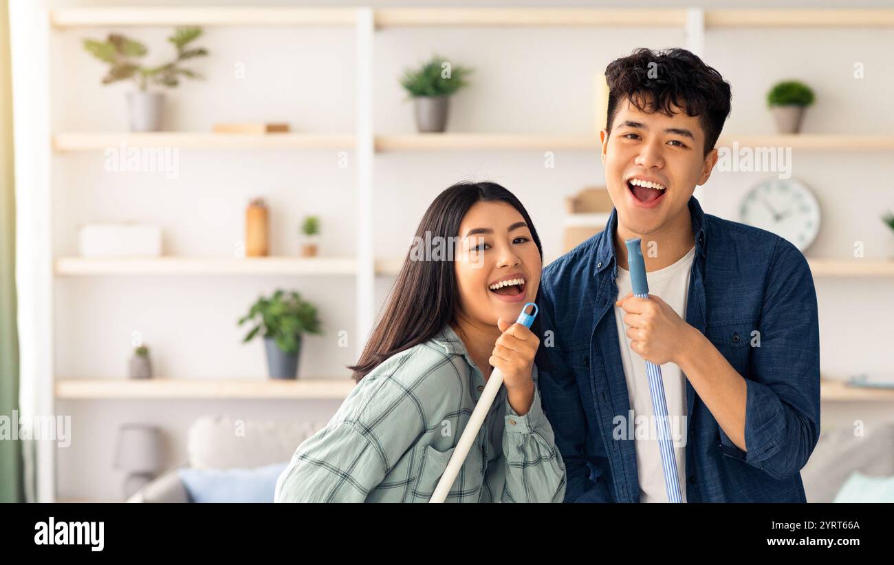 Positive chinese lovers having fun while cleaning house Stock Photo