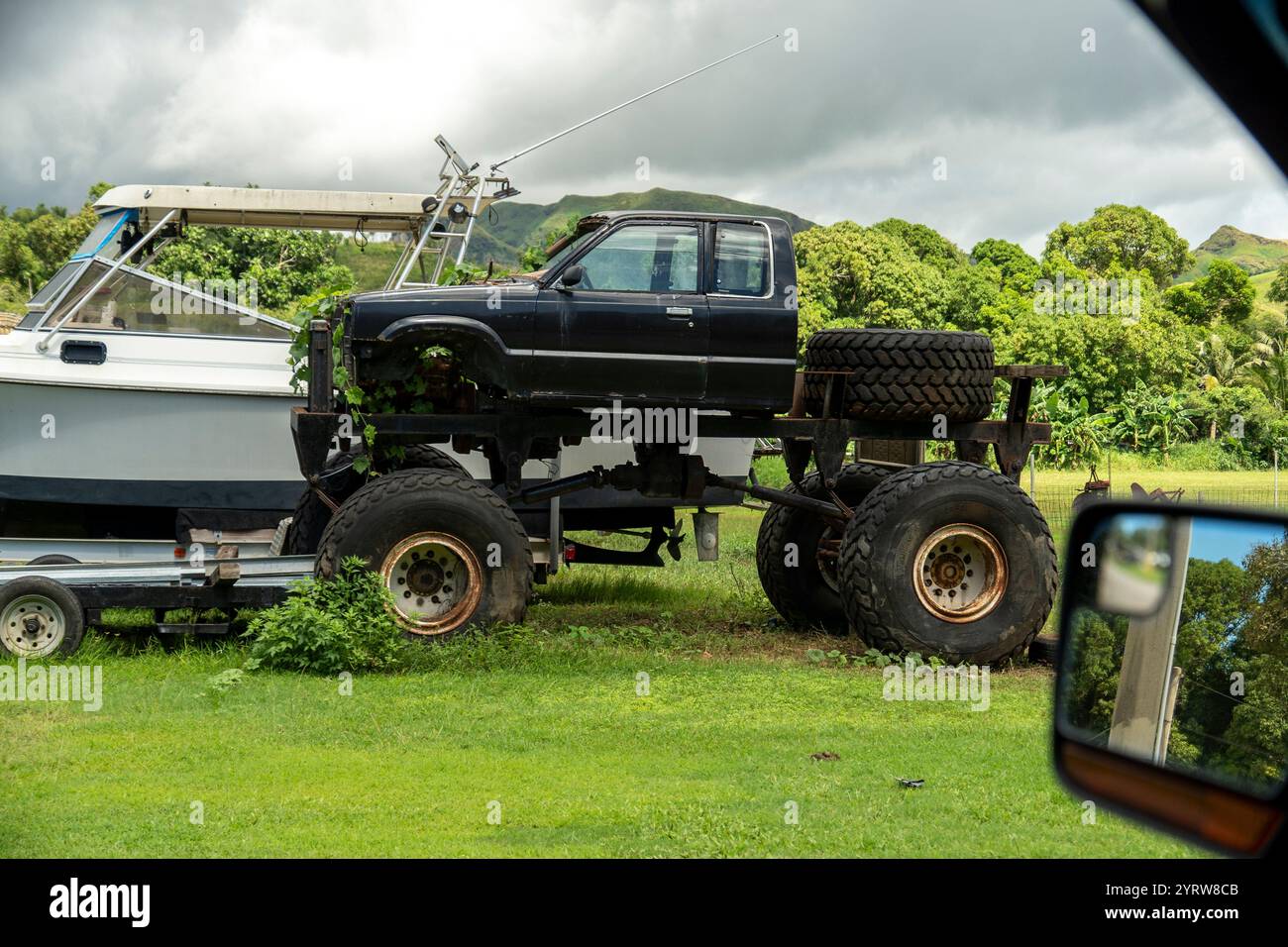 Modified truck on large tires parked beside a boat in a grassy area Stock Photo