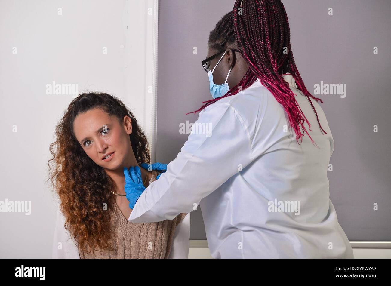 Female doctor wearing gloves and mask examining female patient's neck in medical office Stock Photo