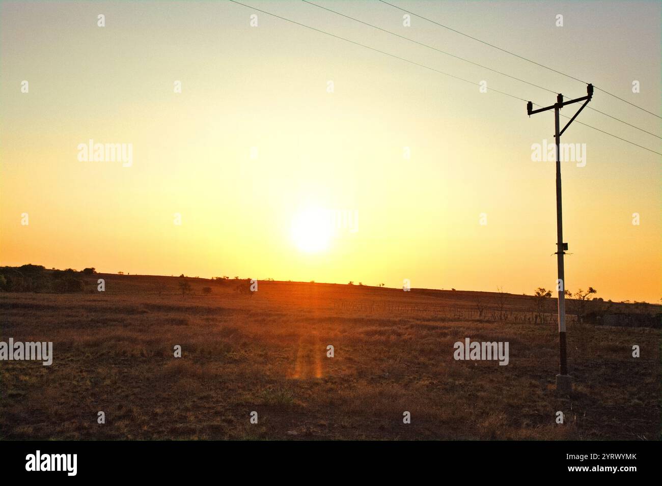Sunset, in a foreground of savanna and an electricity post during dry season in Kanatang, East Sumba, East Nusa Tenggara, Indonesia. Stock Photo