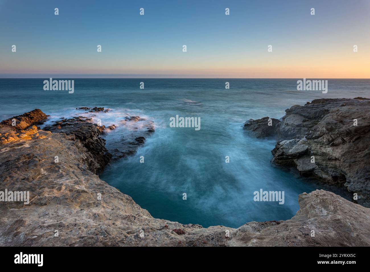 Waves gently crash against rocky cliffs at Leo Carrillo State Beach as the sun sets, creating a serene and picturesque coastal view. Stock Photo