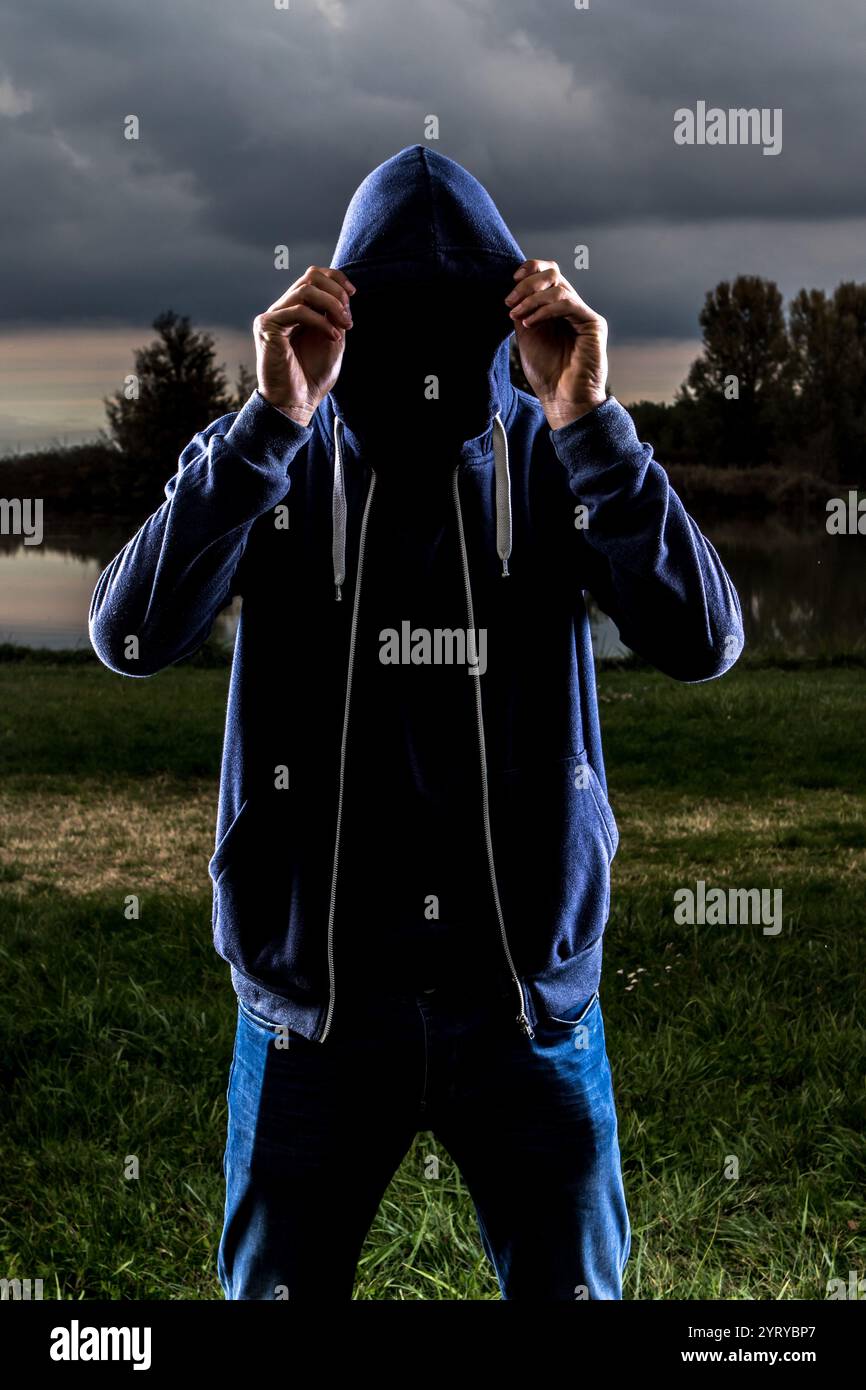 Mysterious hooded man covering his face with his hands in a dramatic ...