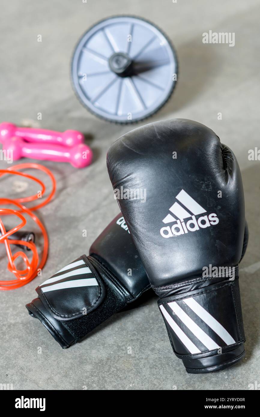 Black Adidas boxing gloves resting on the floor next to an ab roller, symbolizing strength training, fitness, and combat sports. Stock Photo