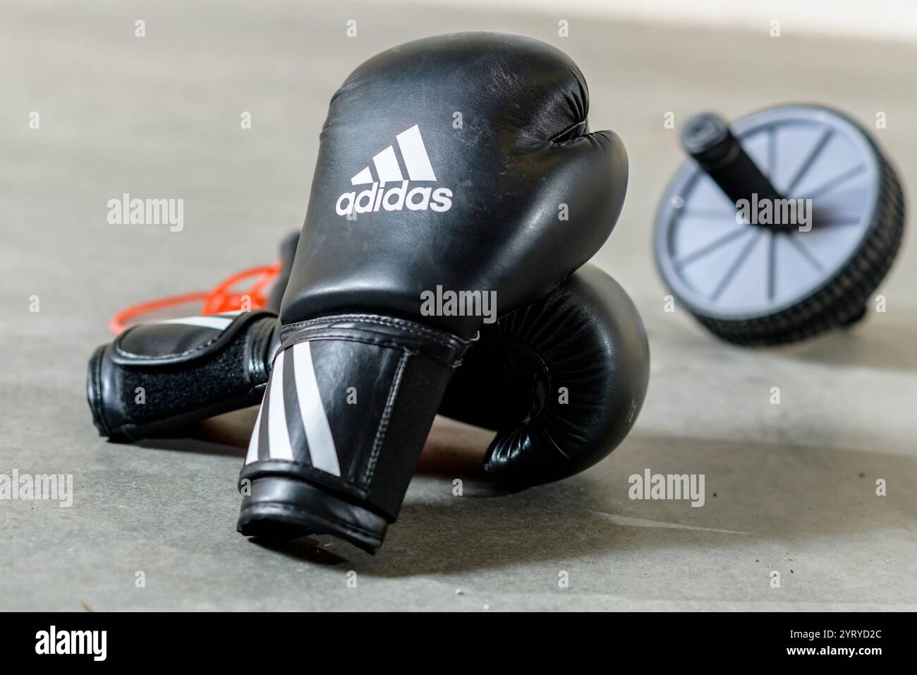 Black Adidas boxing gloves resting on the floor next to an ab roller, symbolizing strength training, fitness, and combat sports. Stock Photo