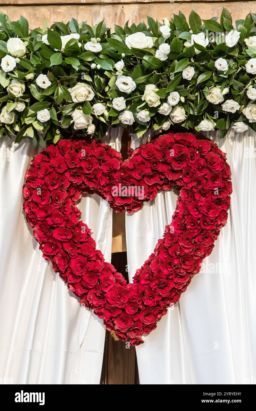 Heart-shaped decoration made of red roses hanging on white curtains ...
