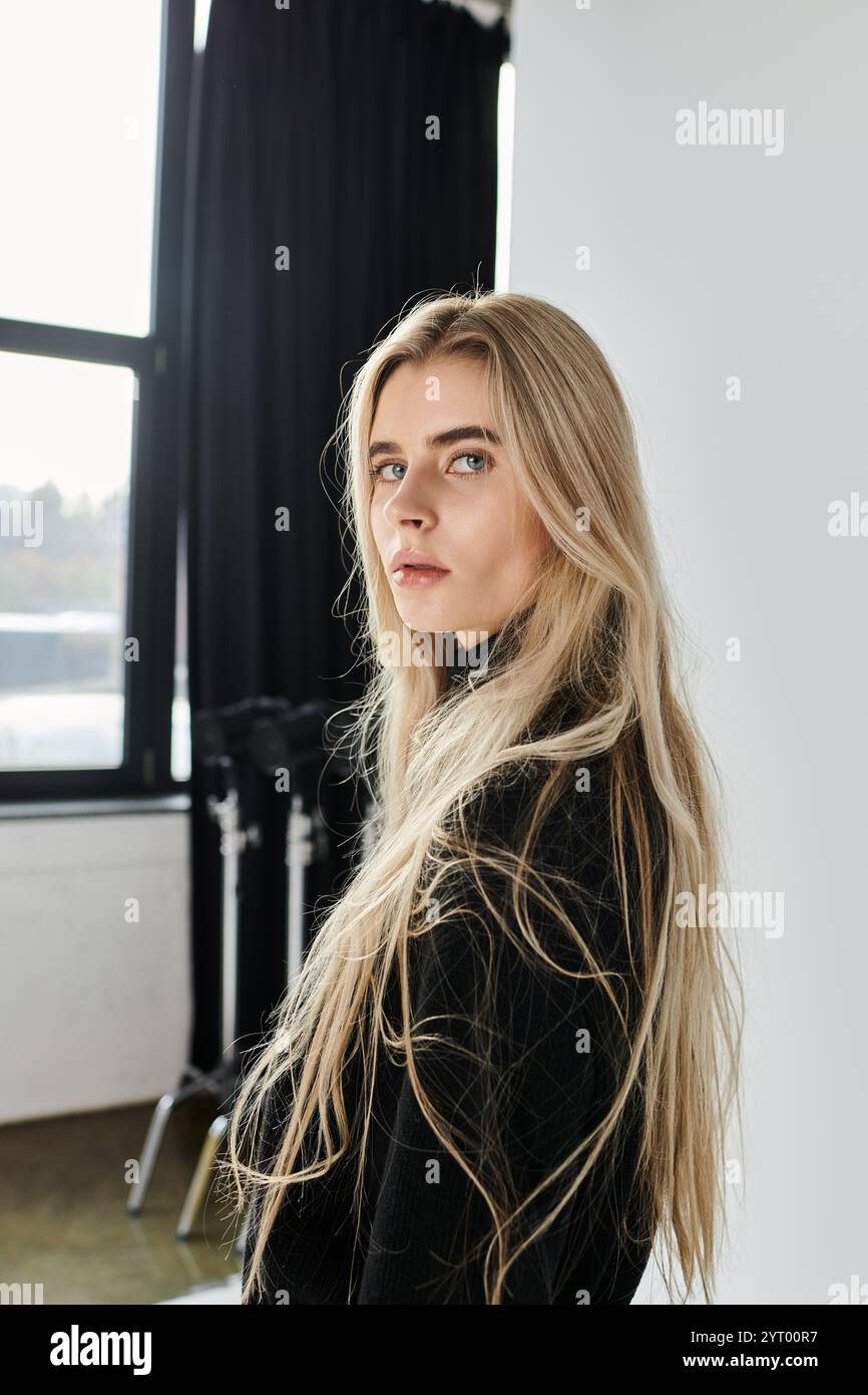 A young woman with long blonde hair poses elegantly in a chic black ...