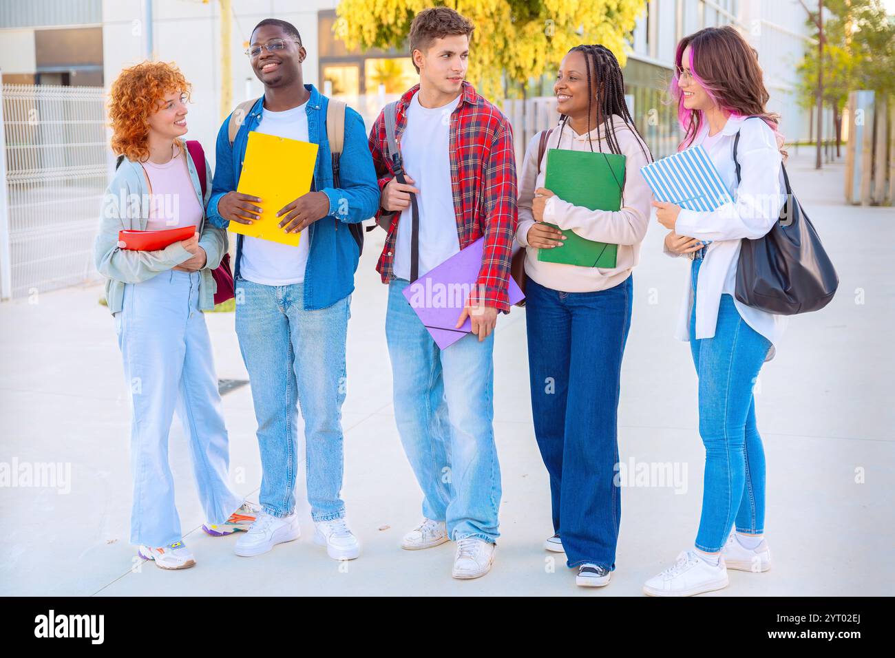 Diverse group of students smiling and walking together outdoors with notebooks Stock Photo