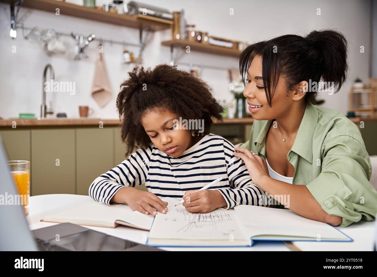 A mother helps her daughter draw and bond in their bright kitchen one ...