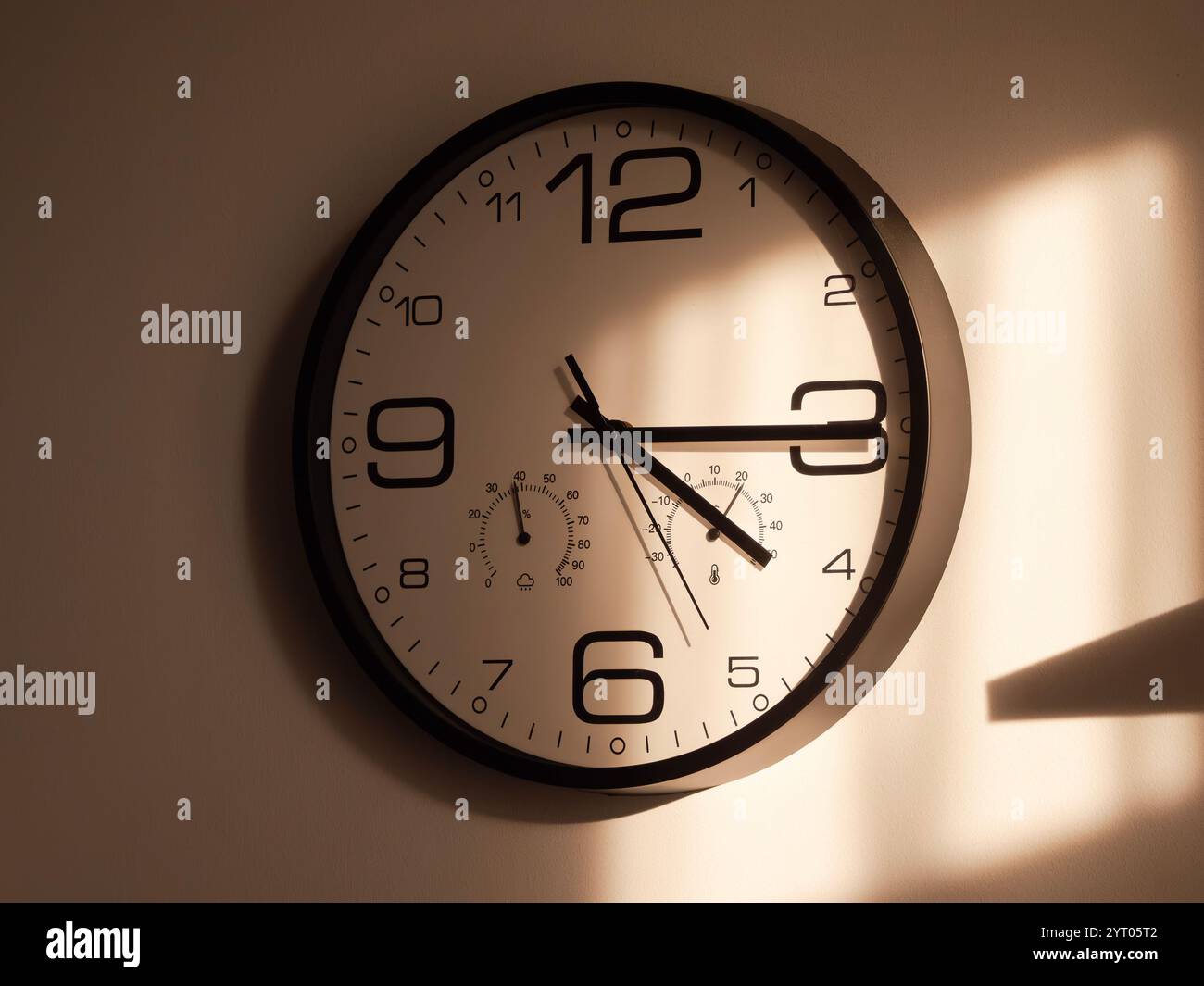 A round wall clock shows the time while warm sunlight creates beautiful ...