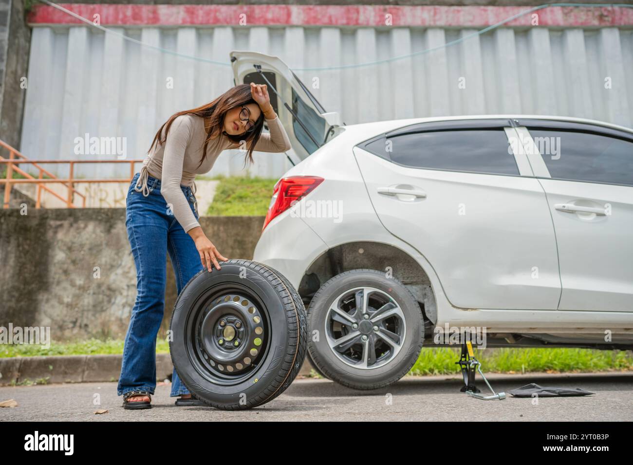 A woman is changing a flat tire by her car while parked on the roadside ... - Changing A Flat Tire On A Car