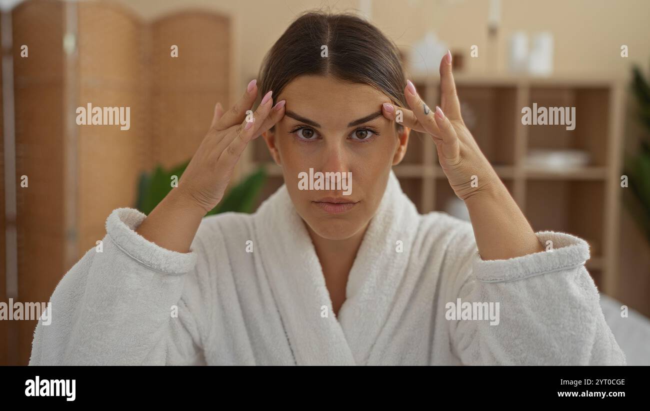 Young woman in spa wearing white robe while massaging her temples ...