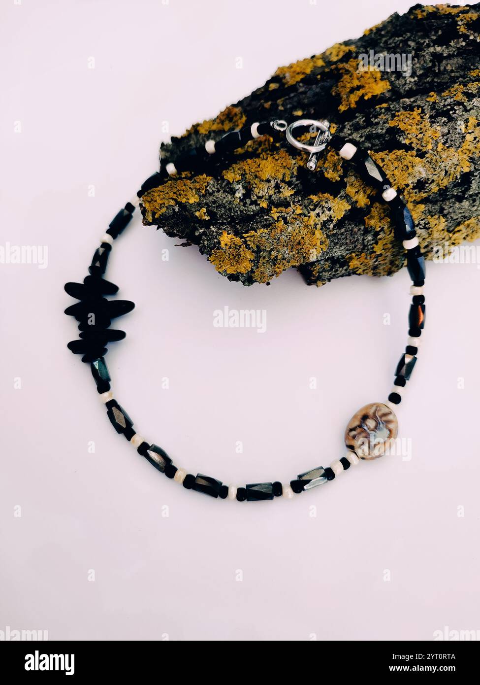 Black stone beaded necklace at pink background close up on tree bark with lichen arrangement. Hematite, magnetite semiprecious stone choker Stock Photo