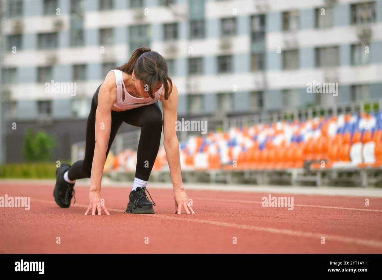 A fit woman crouches at the starting line, her muscles tense and ...