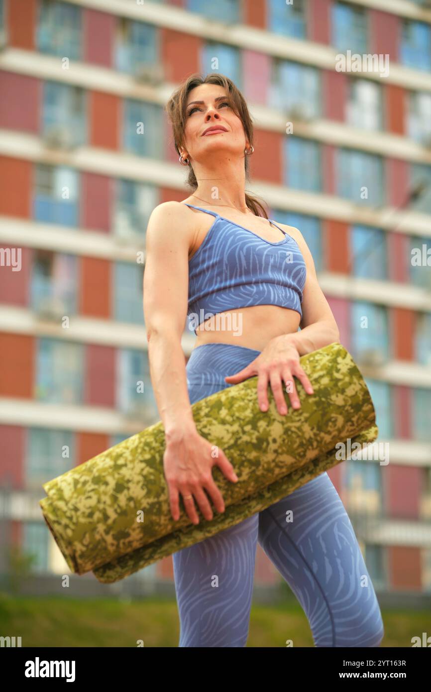 Holding a yoga mat in an urban environment, the woman in blue sports ...
