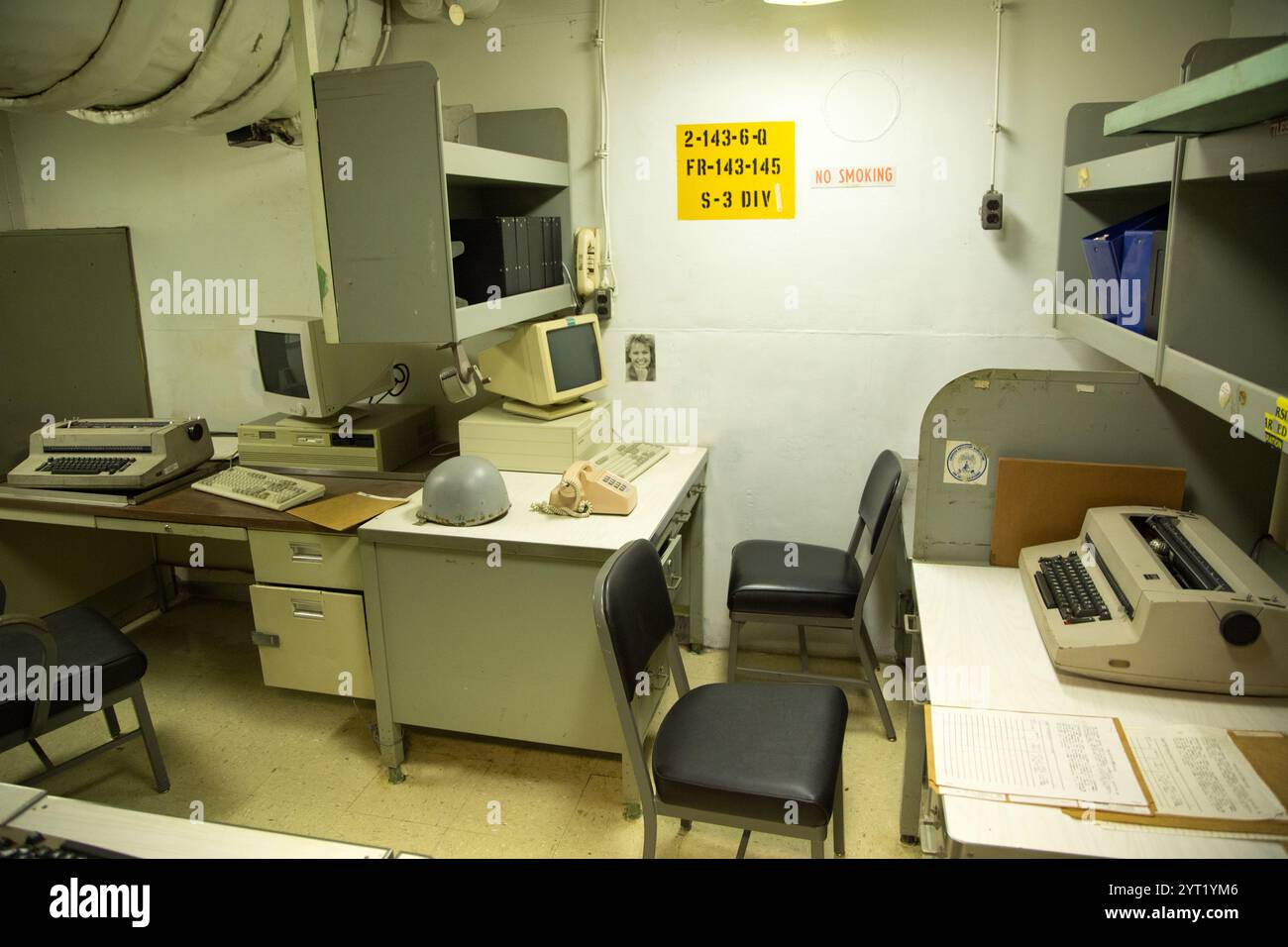 A room with a desk and two chairs, one of which has a yellow sign on it that says '2-10-4' Stock Photo