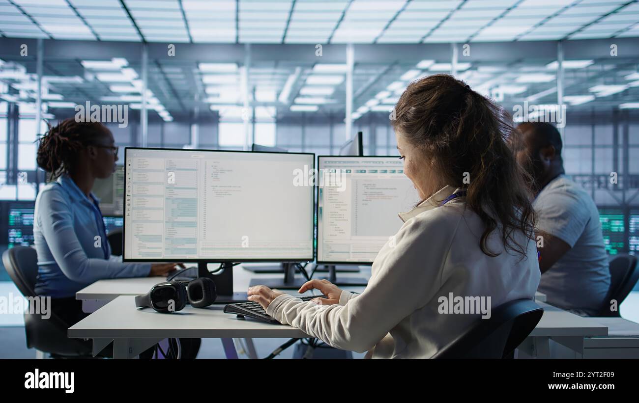 Smiling manager in server hub using computer to find firewall misconfigurations affecting rackmounts performance. Upbeat supervisor checking systems bottlenecks affecting data transfer rates, camera B Stock Photo