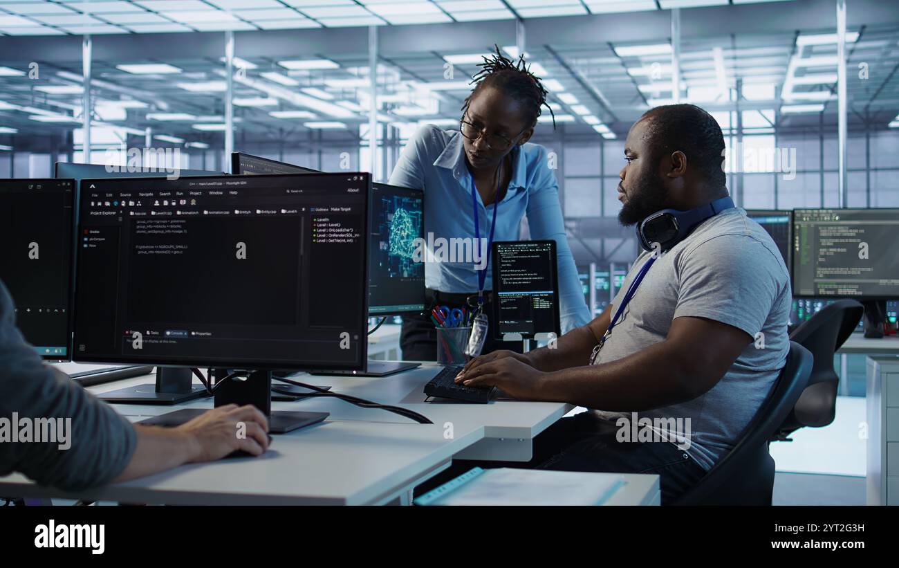 Engineer working with colleague on computer in high tech data center establishment monitoring hardware energy consumption. Team of technicians using PC to check for system failures, camera B Stock Photo