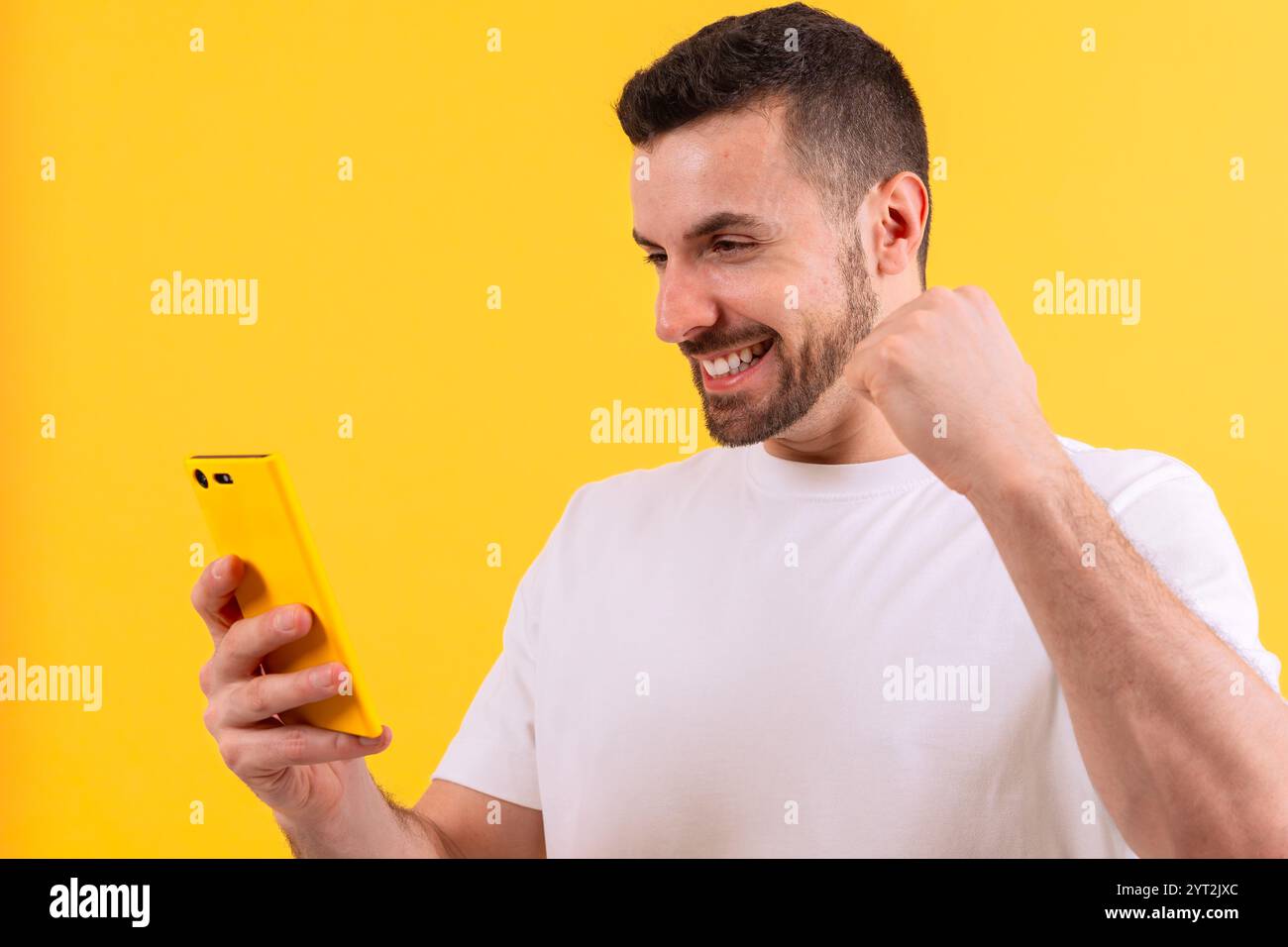 Excited man celebrating success while using smartphone on yellow background Stock Photo