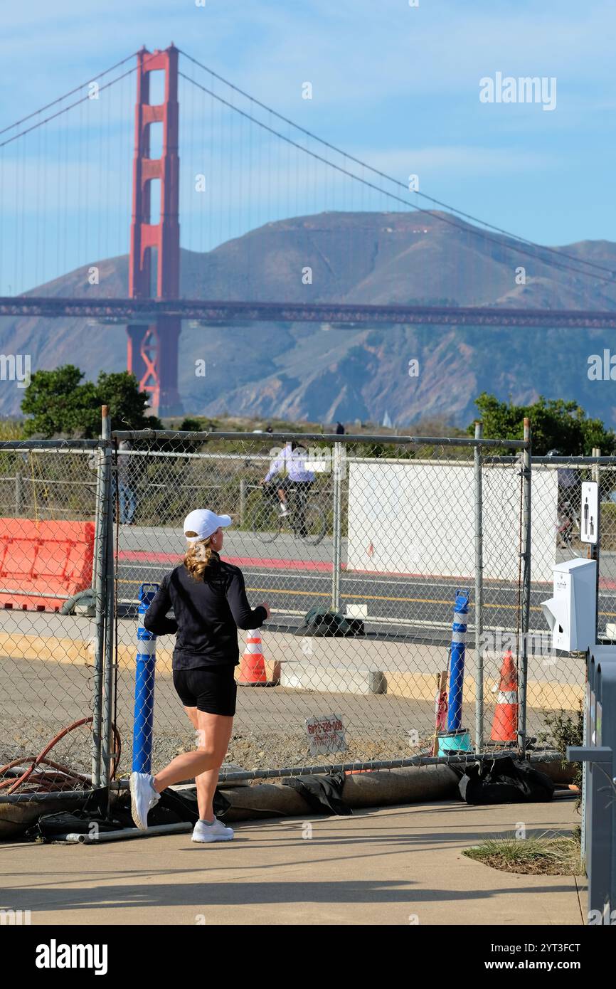 A lone female jogger running on a path at Tunnel Tops park, The Presidio, San Francisco, California with a view of the Golden Gate Bridge. Stock Photo