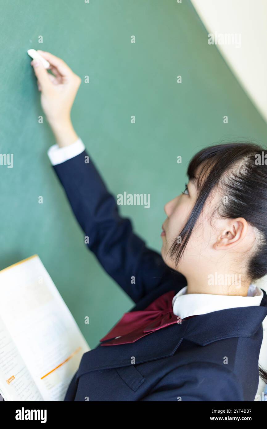 Female high school student writing on blackboard Stock Photo