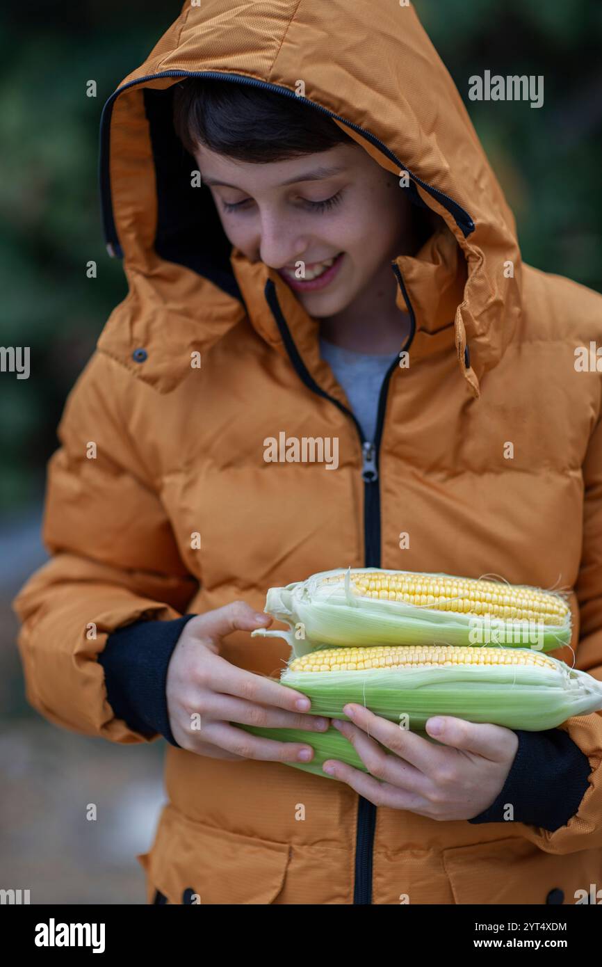 Boy in winter jacket holding several corn cobs in hands Stock Photo