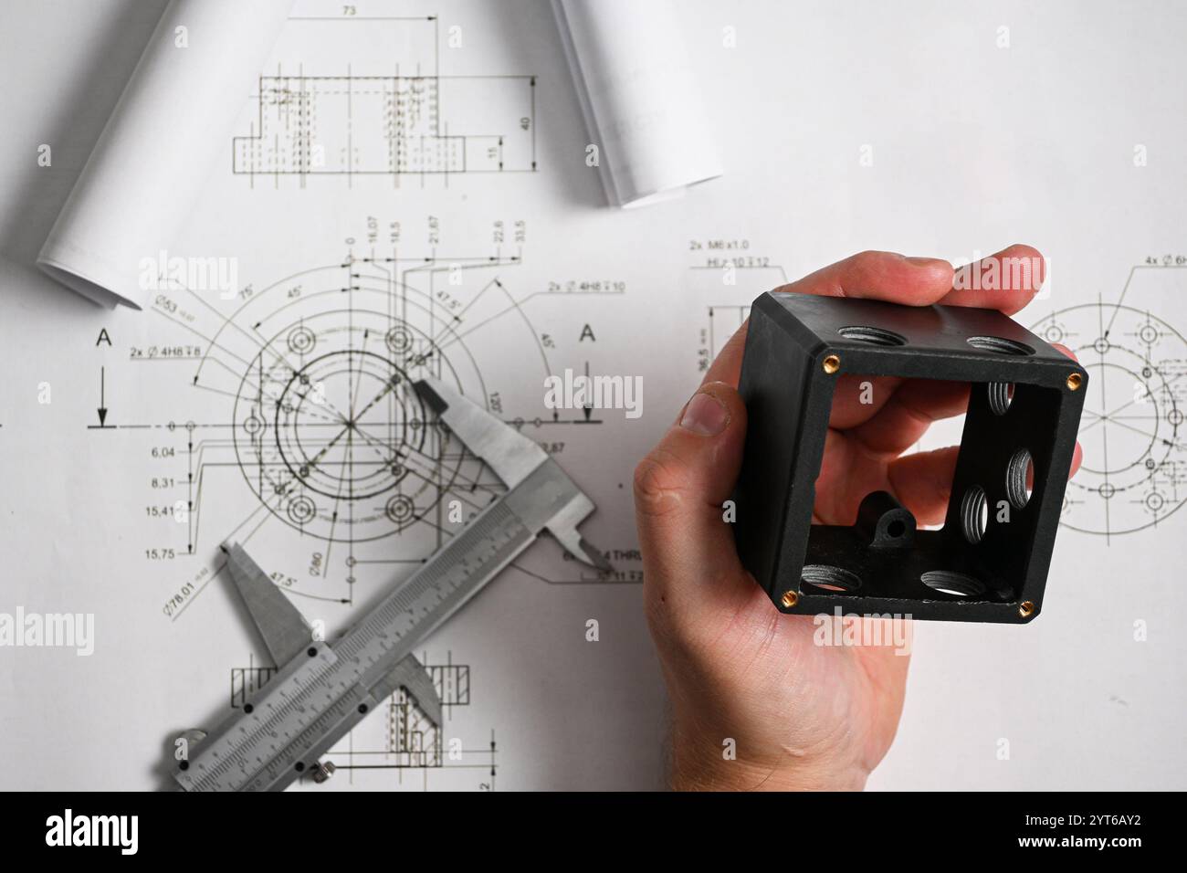 Engineer comparing a plastic component with its technical drawing using a caliper, ensuring precise measurements and quality control. Stock Photo