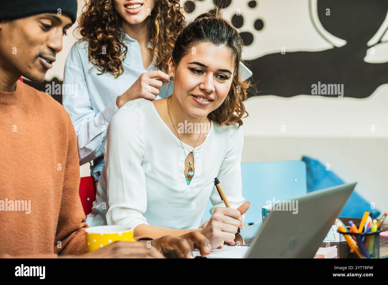 Three colleagues collaborating on a project, using a laptop and taking notes Stock Photo