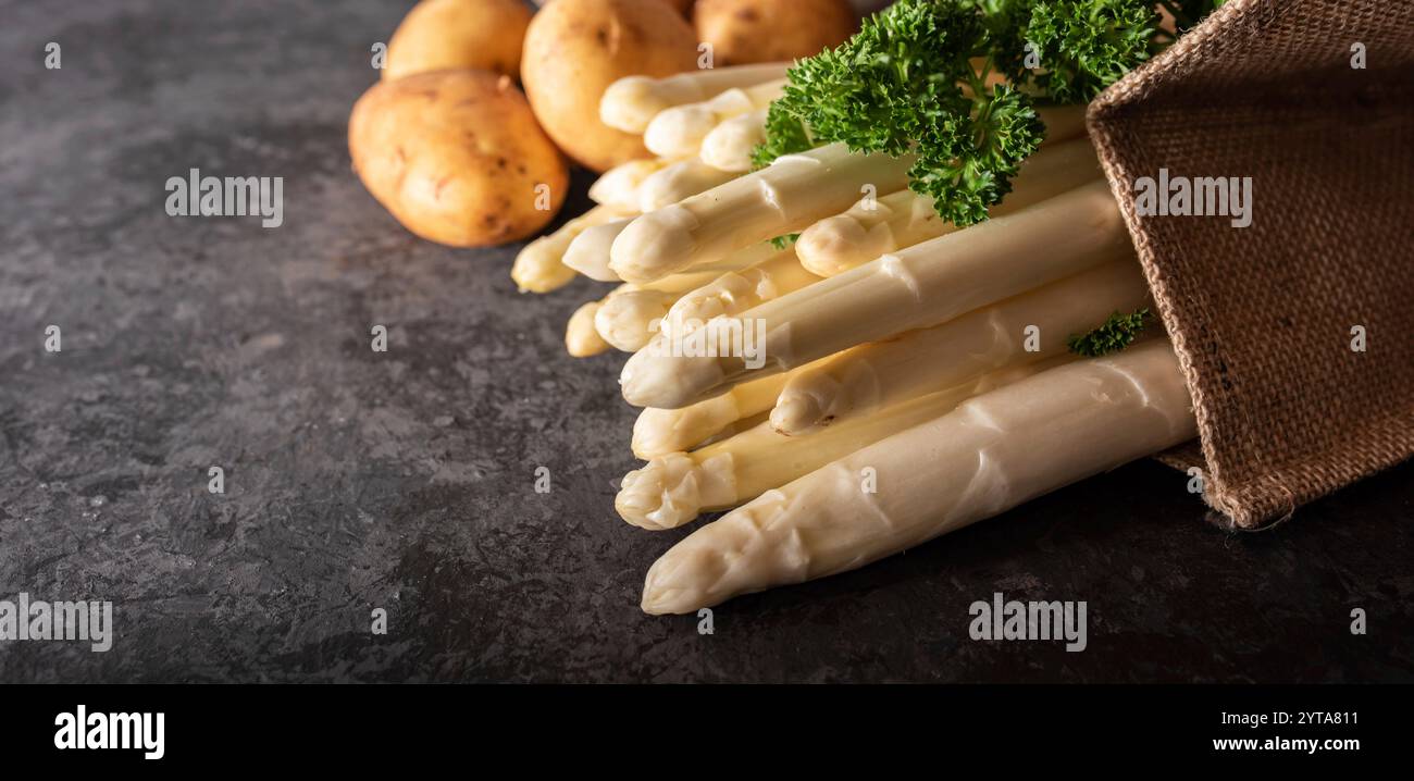 Fresh white asparagus and raw potatos in a shopping bag. Seasonal spring vegetables on black slate. Saisonal and healthy gastronomy concept with space for text. Stock Photo
