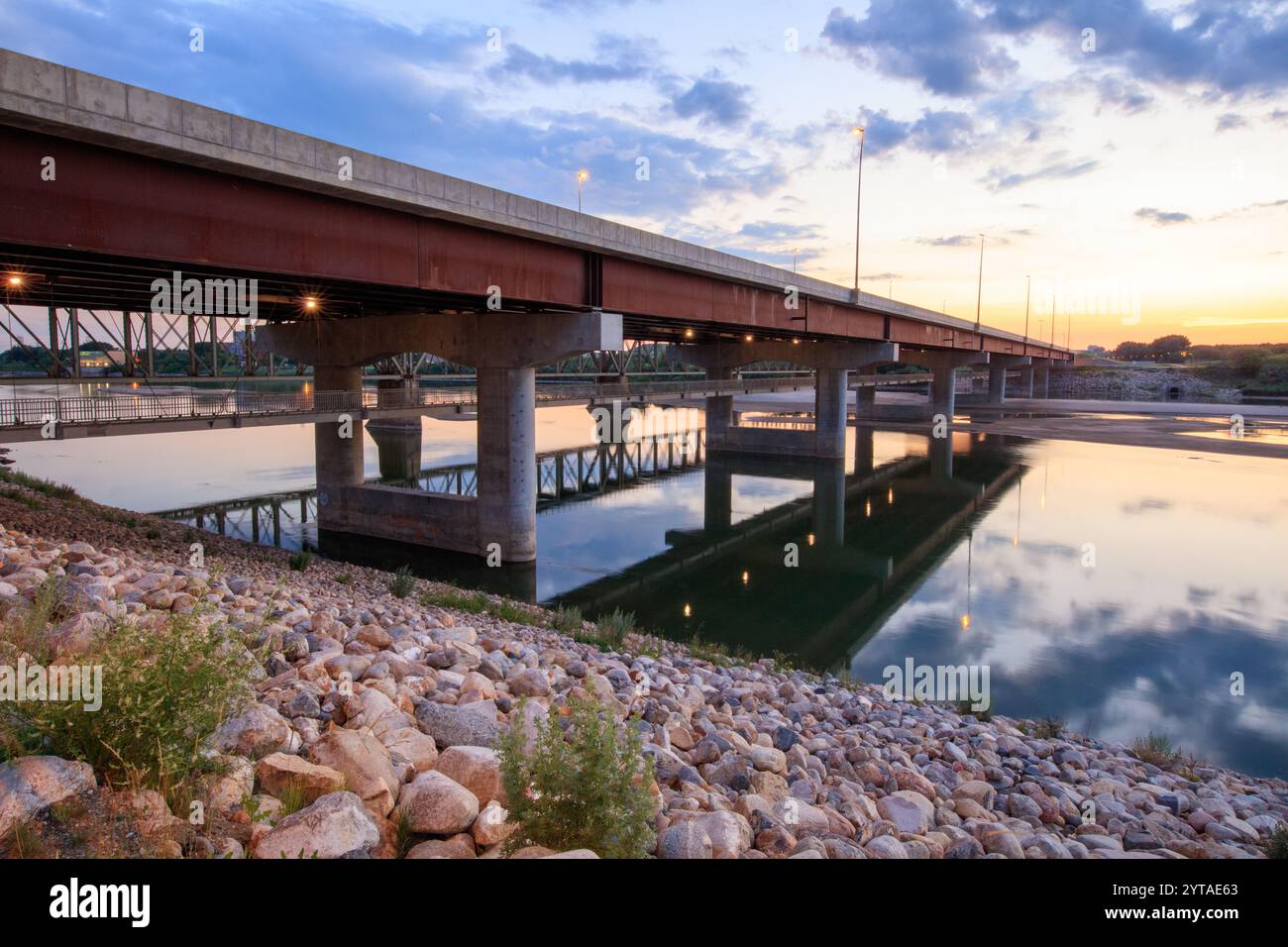 A bridge over a river with a reflection of the bridge in the water. The bridge is lit up at night Stock Photo